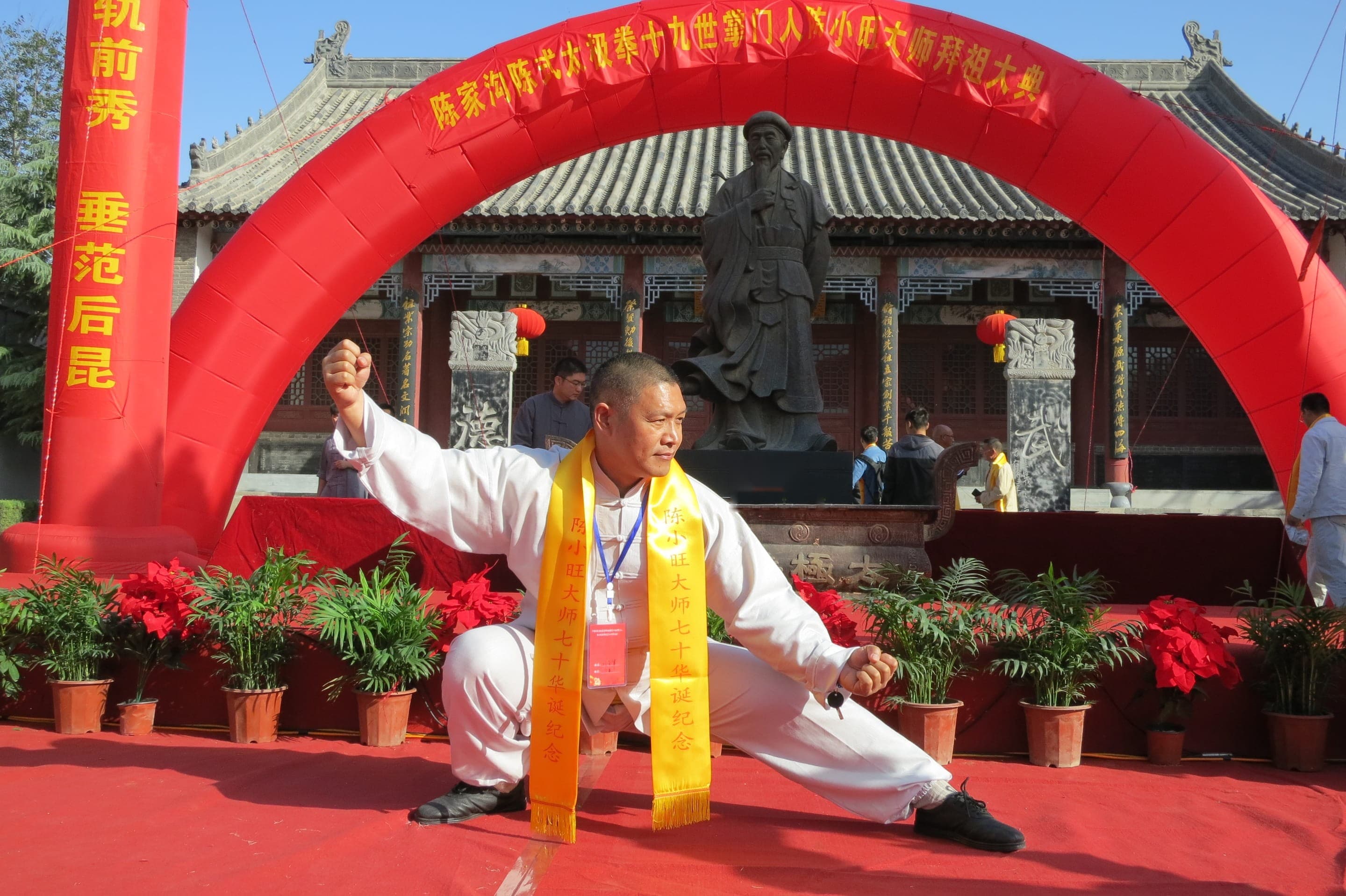 Master Liu Quanjun in a deep pu bu stance in white uniform, before the Chen Wangting statue at Chen Village